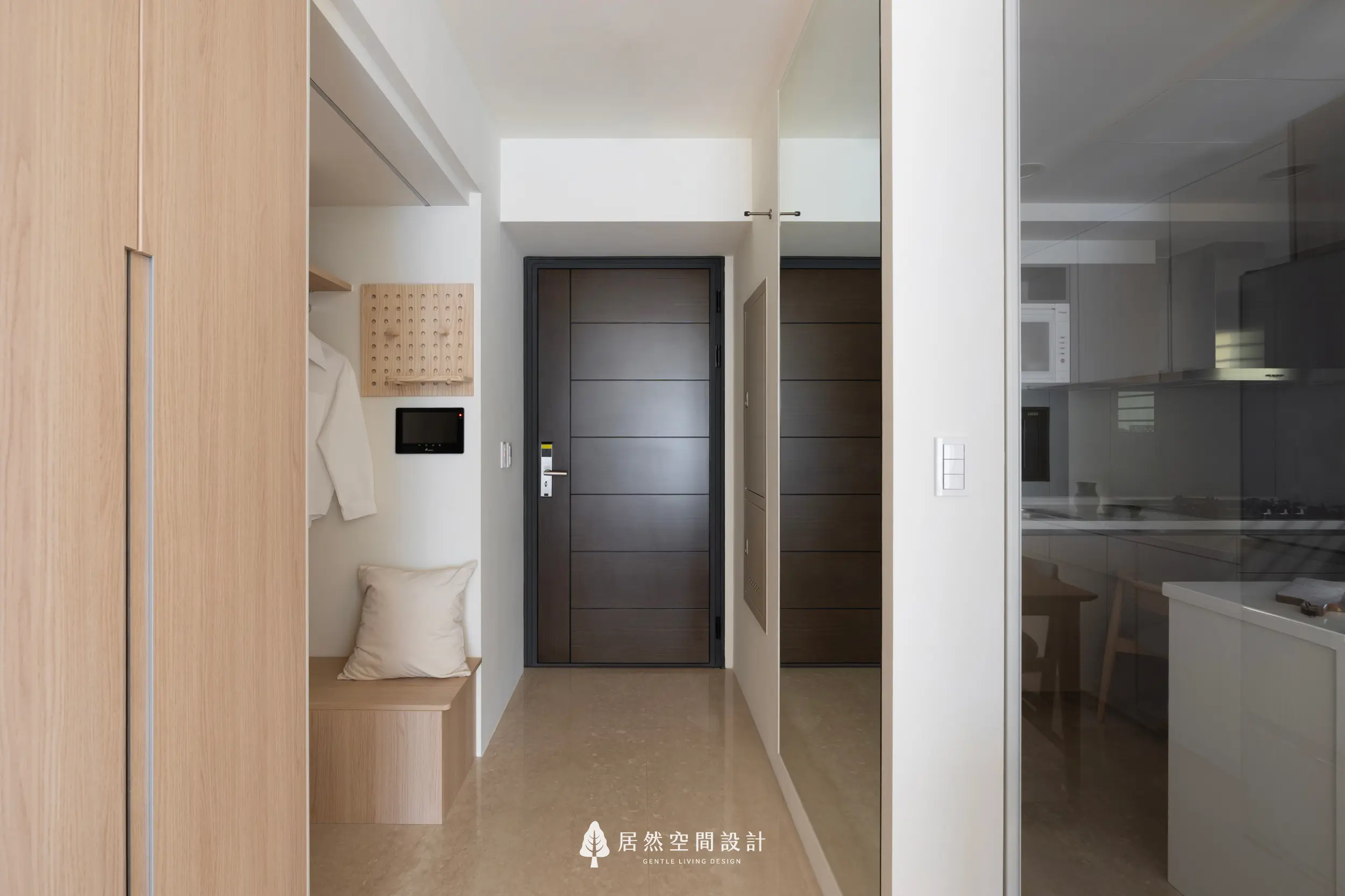 玄關以溫潤木質打造實用落塵區，結合穿鞋椅與展示掛板，讓收納更有秩序；深色大門穩定視覺，右側鏡面延伸空間感，呈現明亮俐落的迎賓動線。