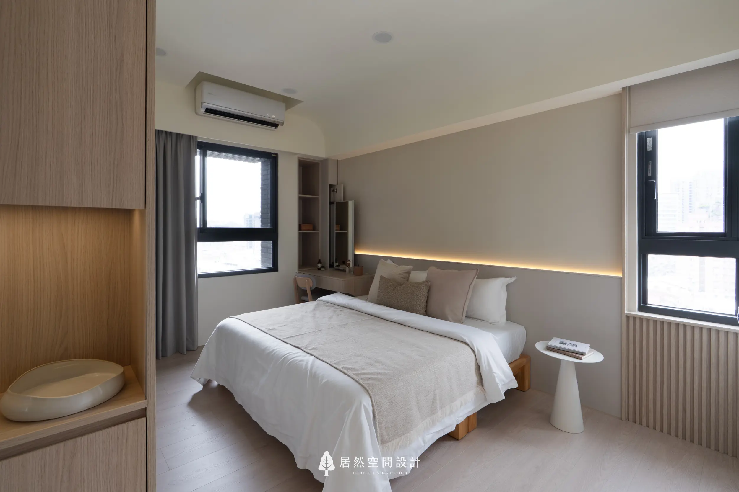 主臥以溫柔米色鋪陳放鬆氛圍，床頭間接燈光延伸整體層次；雙窗引入明亮採光，後方梳妝區以木質調呼應空間語彙，讓臥室呈現安定且細緻的生活感。