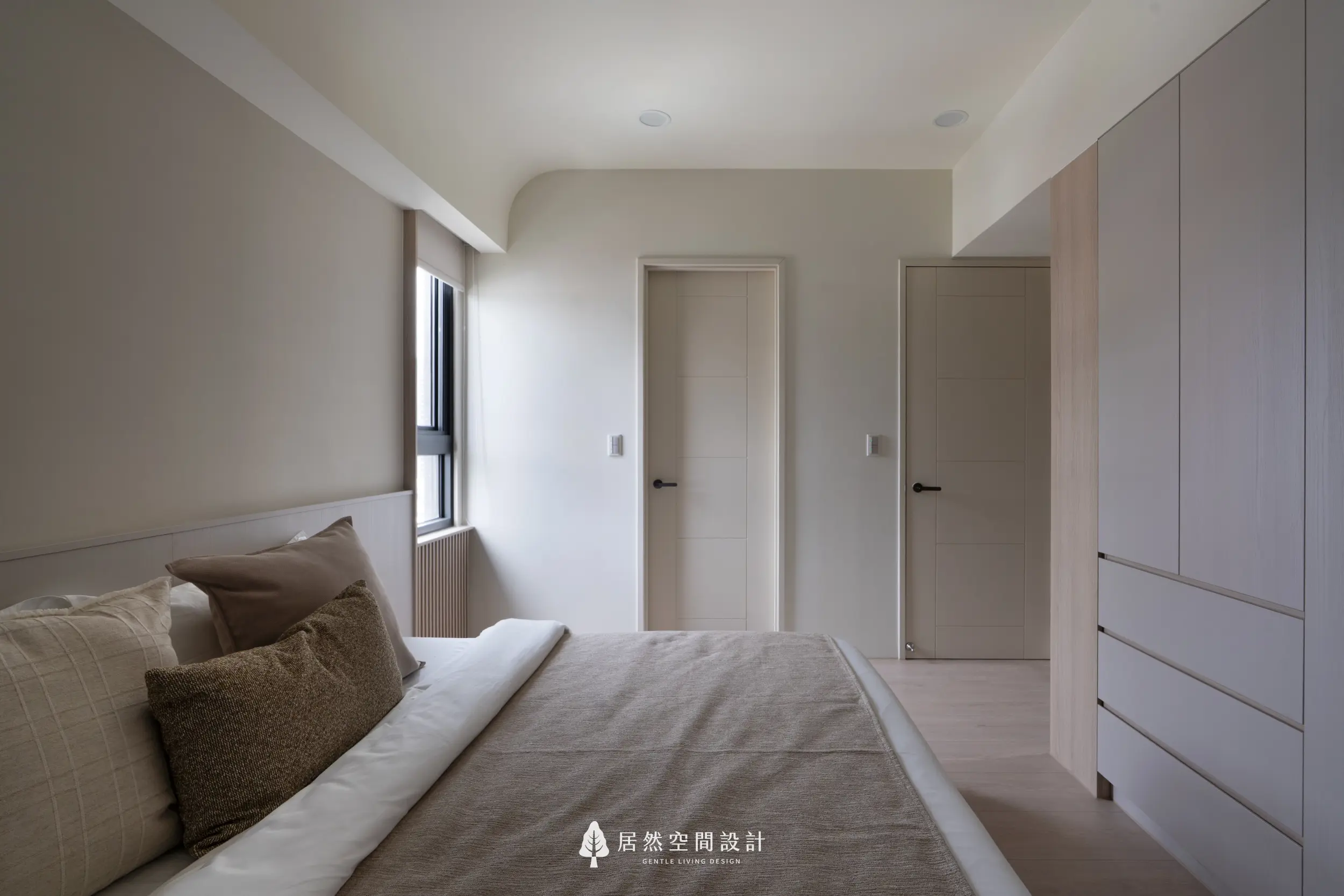 主臥以米白與淡木色營造沉穩舒適的休憩氛圍，左側採光柔和，右側收納櫃體維持整潔，兩道門順暢連接更衣室與衛浴，讓動線自然而安定。