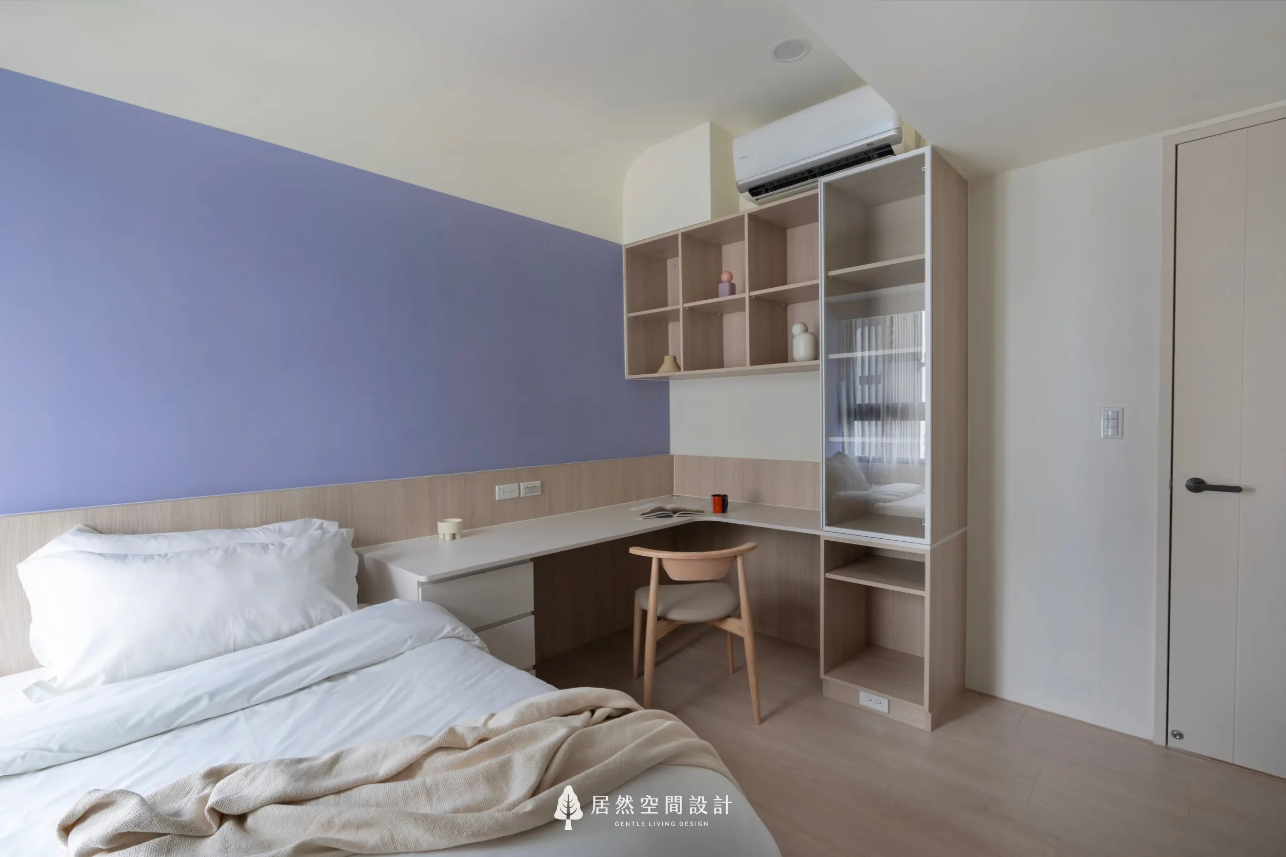 次臥以淡紫色主牆營造柔和氣息，搭配白色床鋪與米色木質層板展現清爽感；轉角書桌結合展示櫃，提供閱讀與收納機能，讓小空間兼具溫度與實用性。