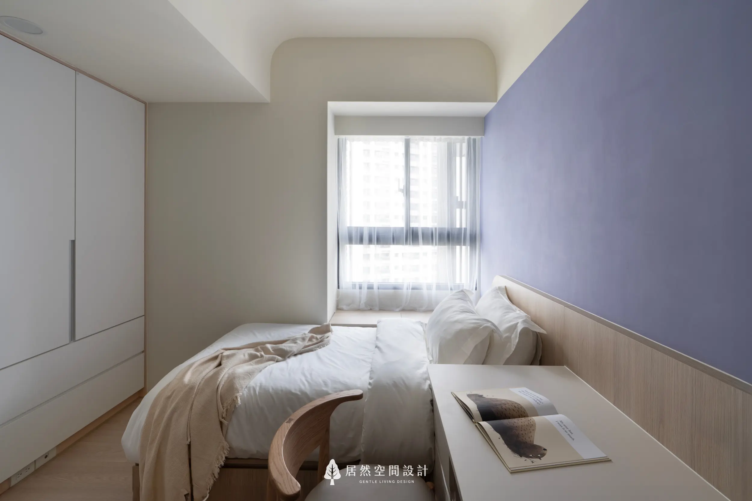 次臥以淡紫主牆與柔白床鋪營造清新氛圍，窗邊透入的自然光讓空間更顯明亮；木質書桌延伸日常使用性，搭配白色衣櫃維持整潔。