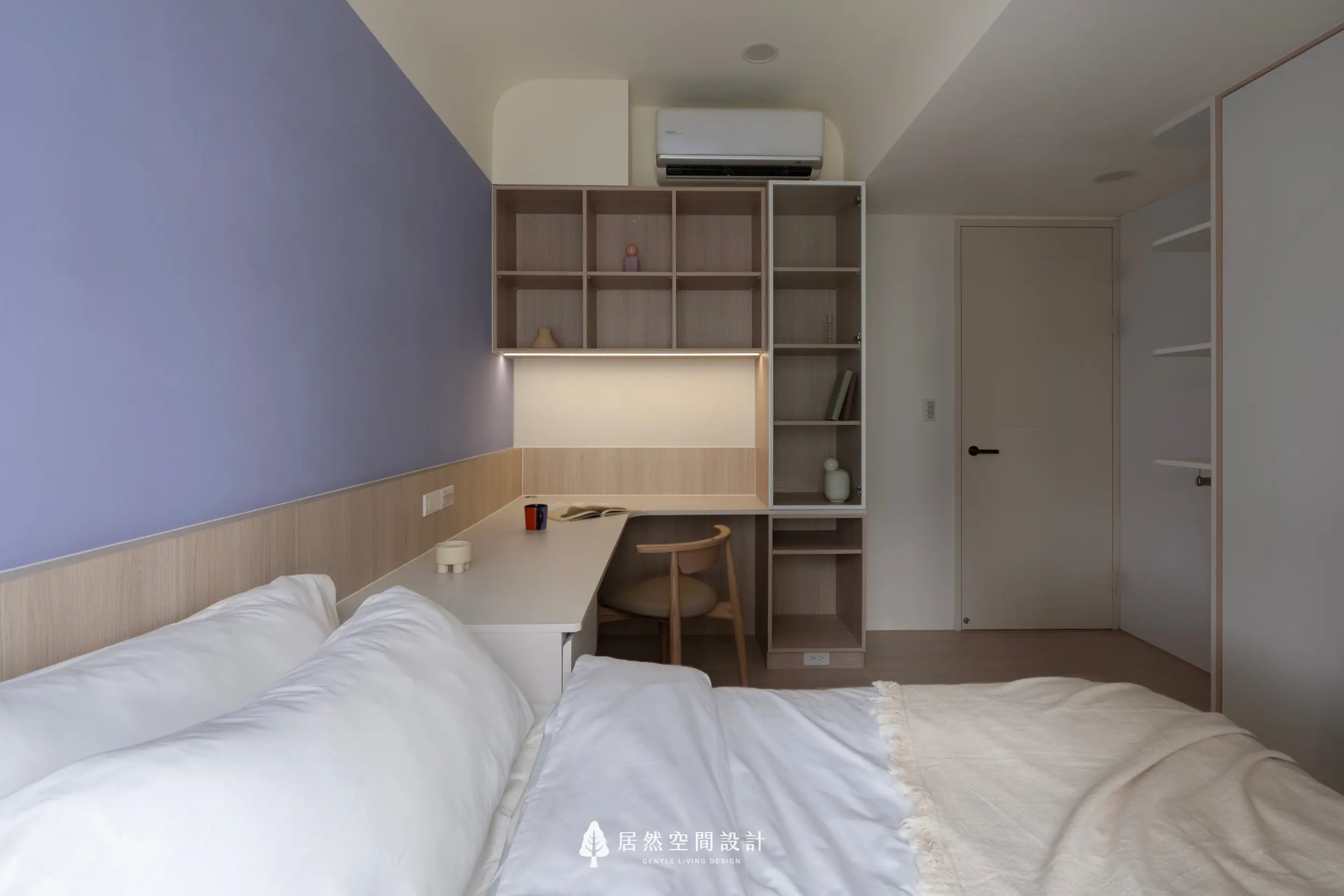 次臥以淡紫色主牆搭配木質書桌，呈現安靜柔和的閱讀氛圍；上方格櫃提供展示與收納，床鋪以白色寢具增添清爽感，整體形式簡潔、溫度適中。
