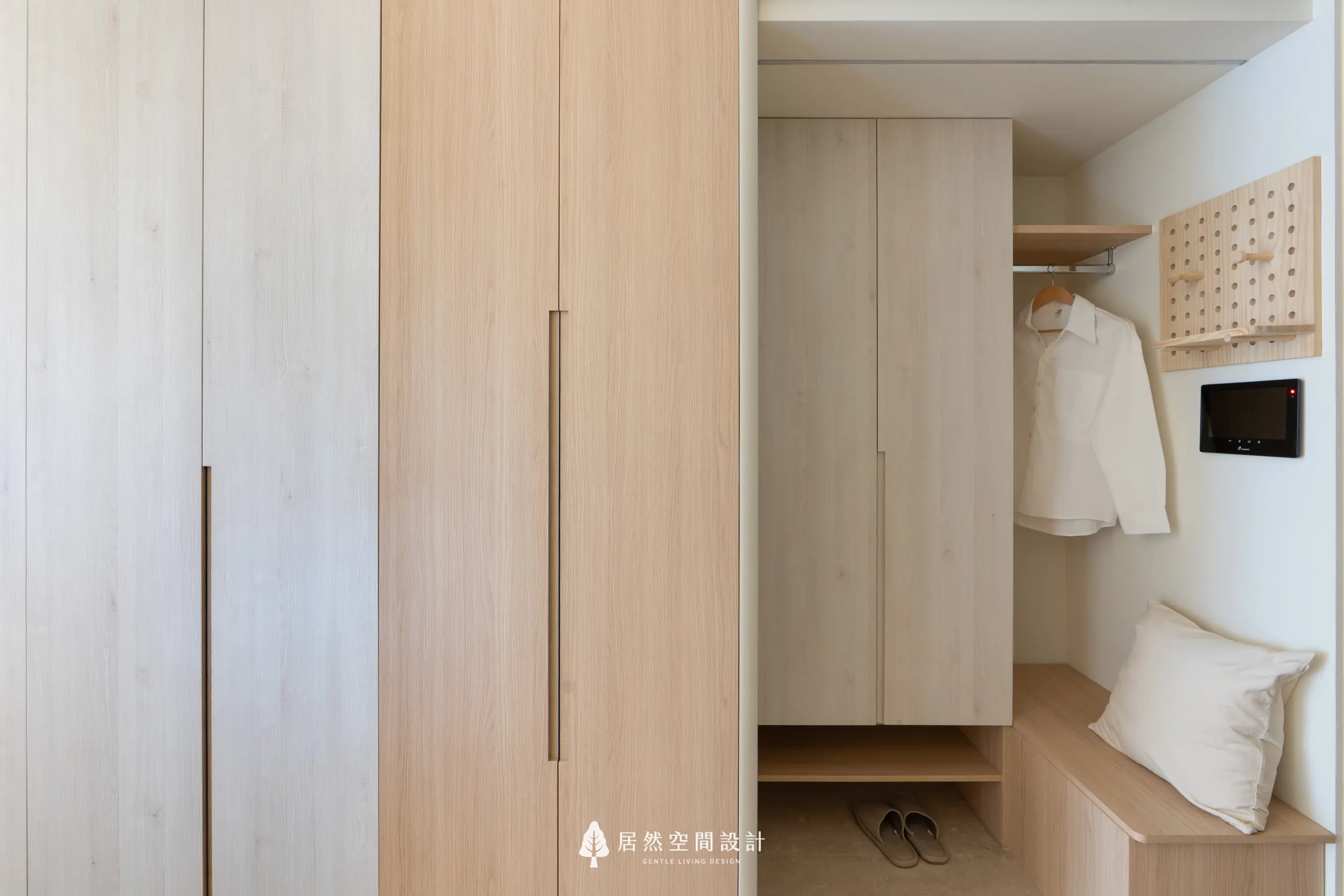 玄關以淺木色櫃體延伸整體一致性，結合吊掛衣物區與穿鞋椅；層板下方留空擺放拖鞋，搭配溫暖靠墊與展示掛板，營造實用又柔和的迎賓角落。