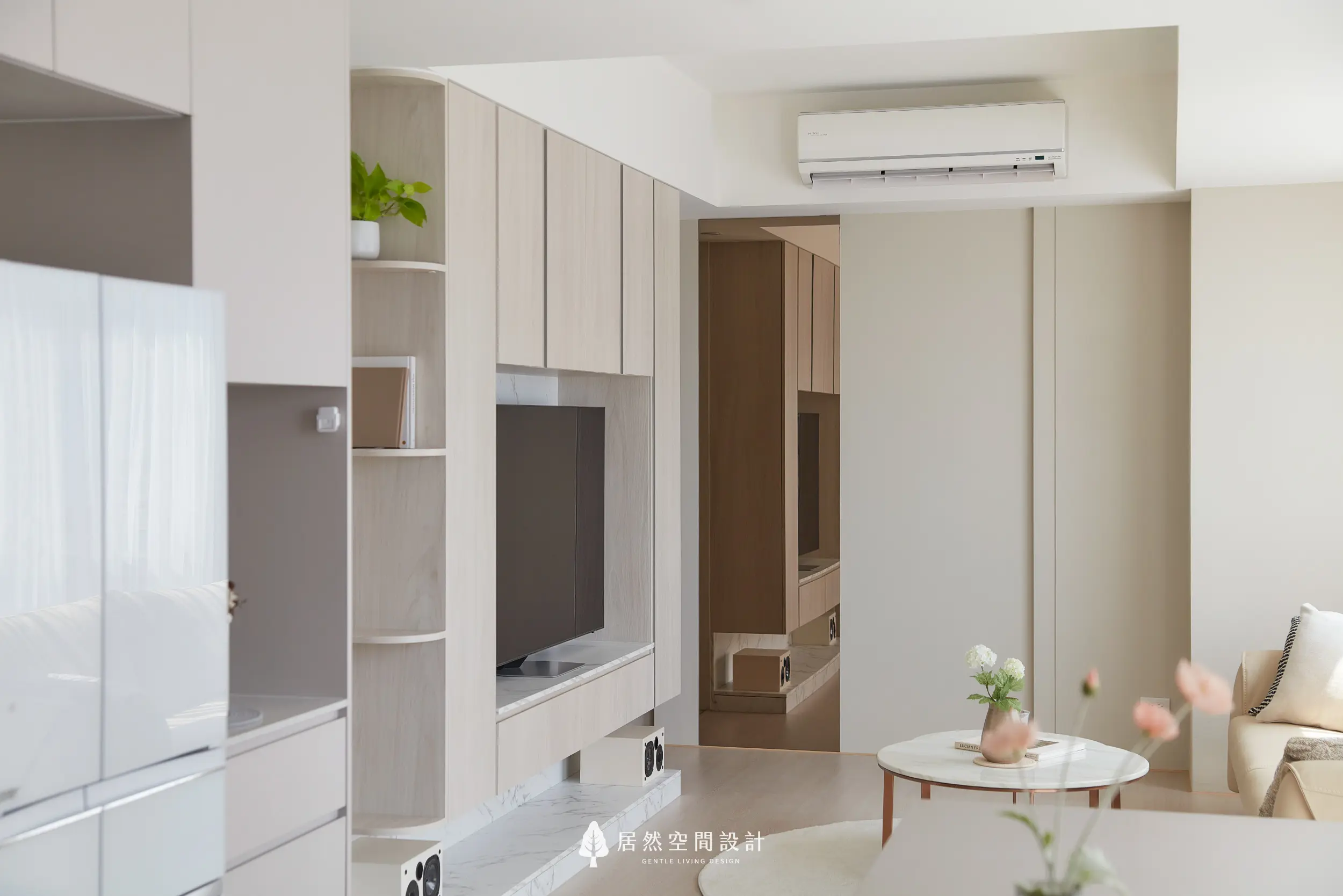 客廳電視牆以淺木櫃體與弧形層架收邊，整合收納與展示，延伸走道動線，搭配柔光層次與大面留白，營造清爽溫潤且視覺放大的公共空間氛圍