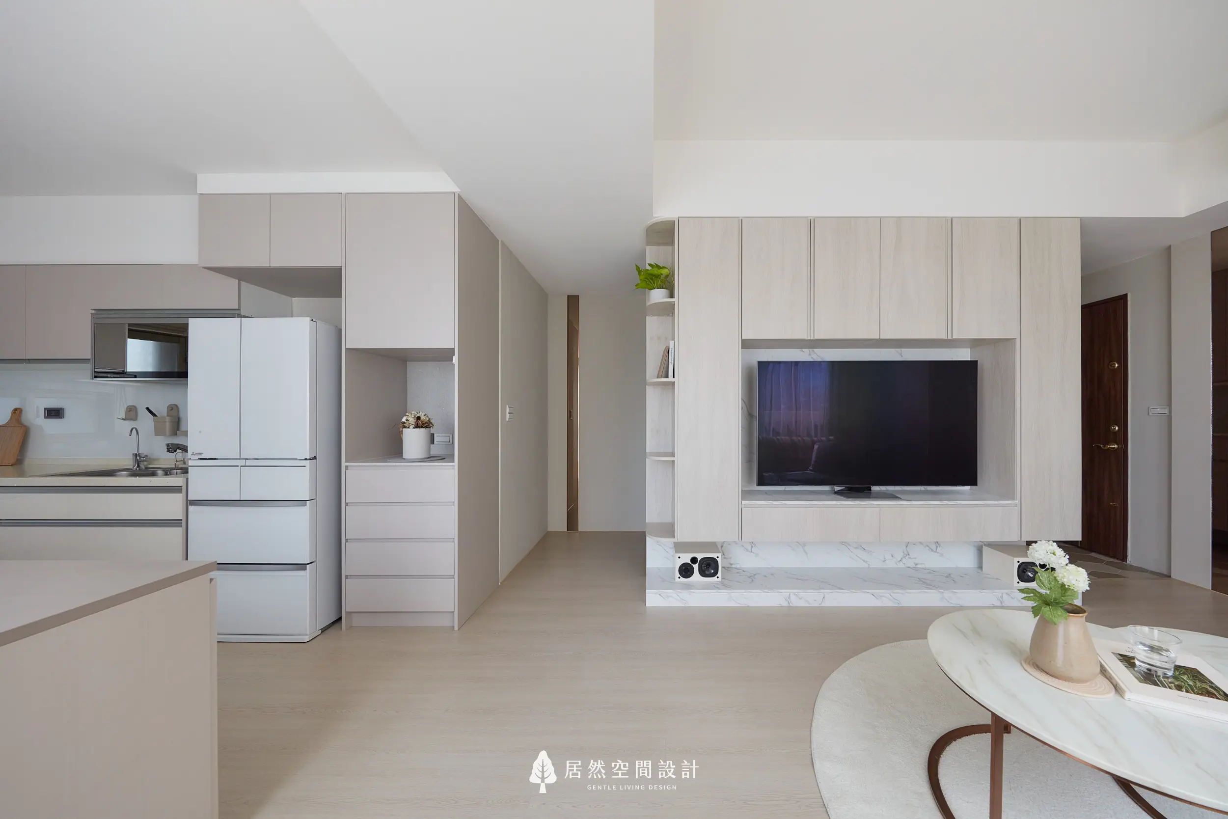 客廳電視牆以淺木系統櫃整合收納，下方石紋平台延伸尺度，銜接餐廚與玄關動線，整體色調柔和一致，展現簡約清爽且實用的公共空間配置