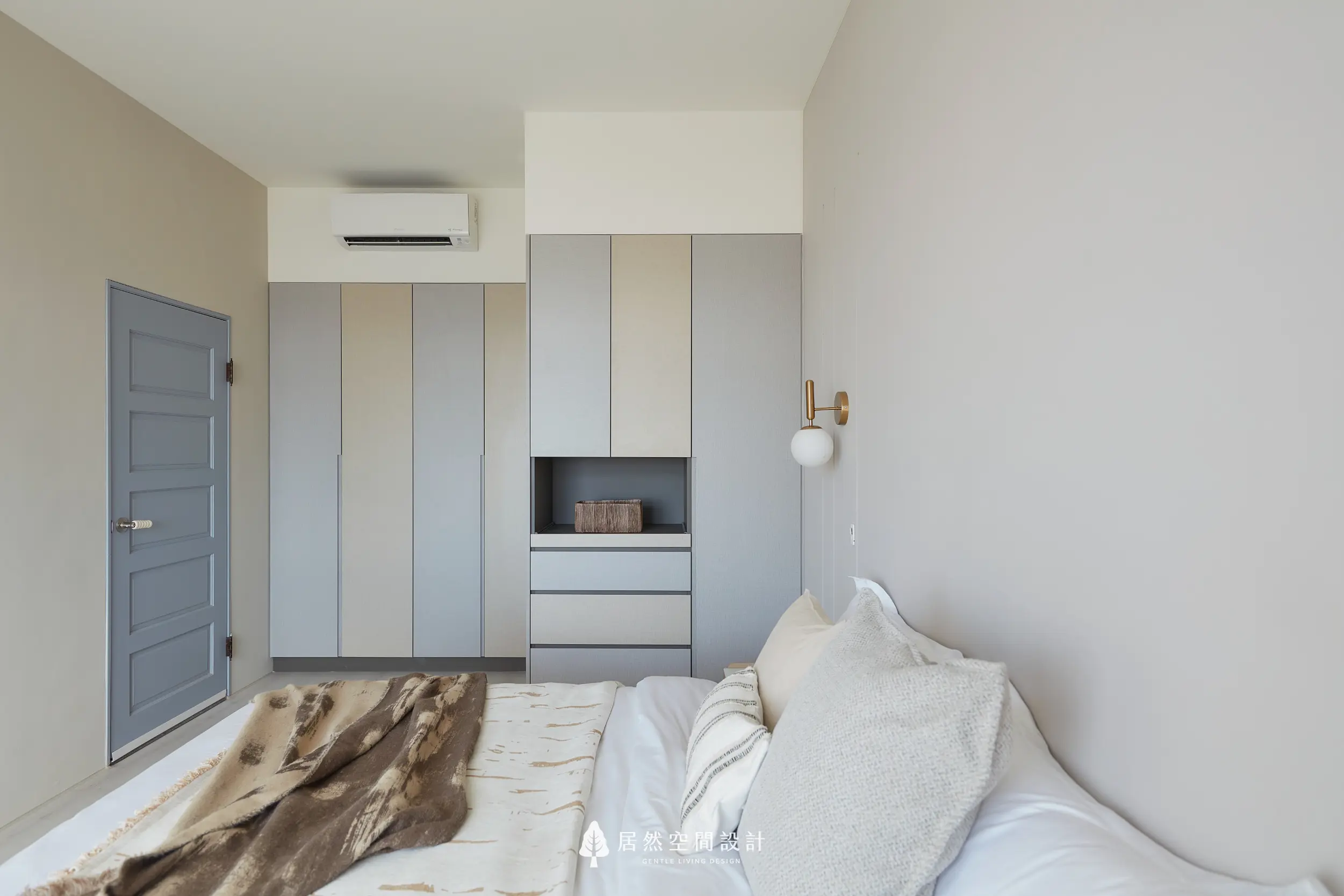 主臥衣櫃以雙色門片垂直分割，整合開放展示層與抽屜收納，搭配柔和牆色與壁燈配置，讓臥室在機能完整下維持清爽安定的睡眠氛圍