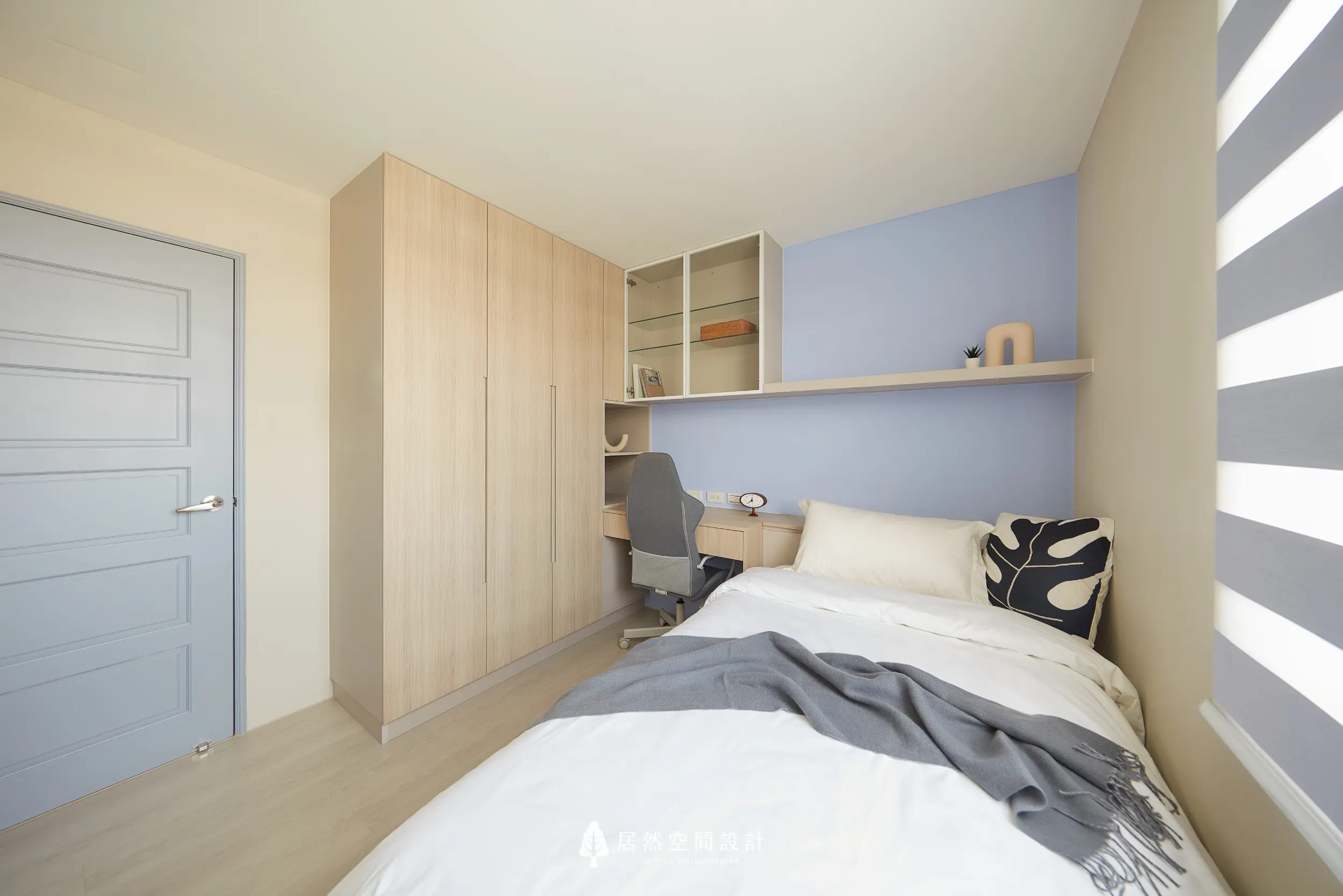 小孩房以淺木衣櫃整合收納，床鋪銜接書桌與展示層，上方層板保留彈性使用，搭配柔和藍紫色牆面，營造安定舒適且利於成長的休憩空間