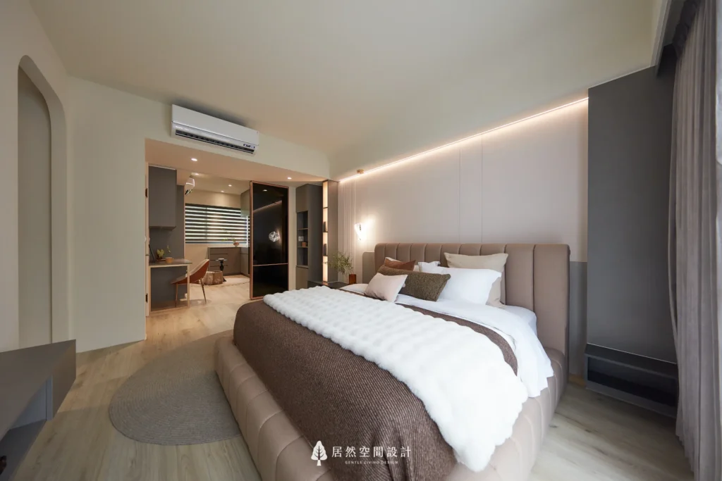 主臥室以米色軟包床頭與雙人床鋪為視覺核心，搭配間接燈帶與柔和牆面營造溫潤氛圍，後方連結書桌與更衣室空間，形塑舒適流動的生活動線