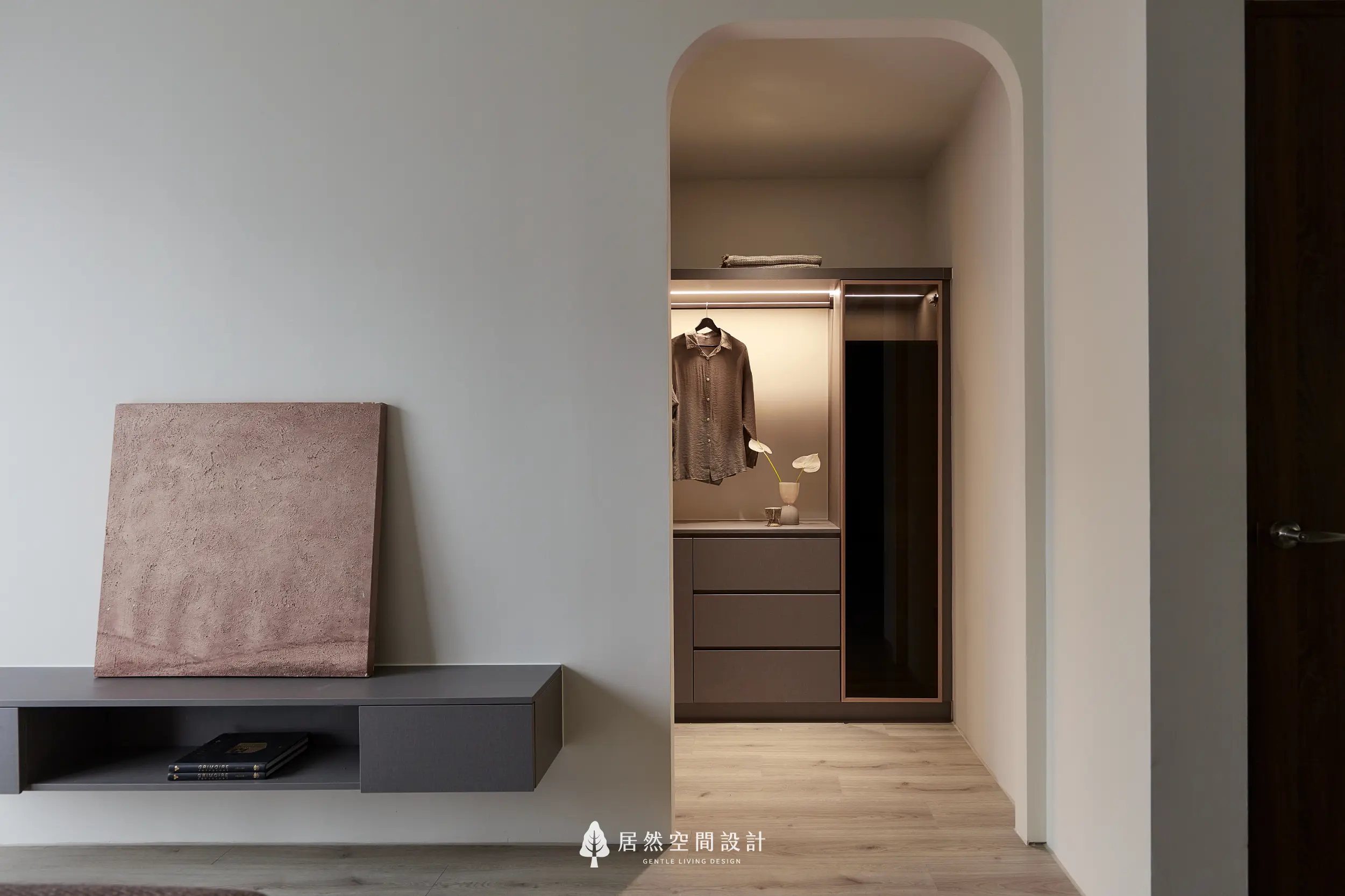 弧形牆面開口界定更衣室入口，內部配置吊掛衣桿與抽屜收納，搭配間接燈光營造柔和展示感，延伸臥室收納與生活動線