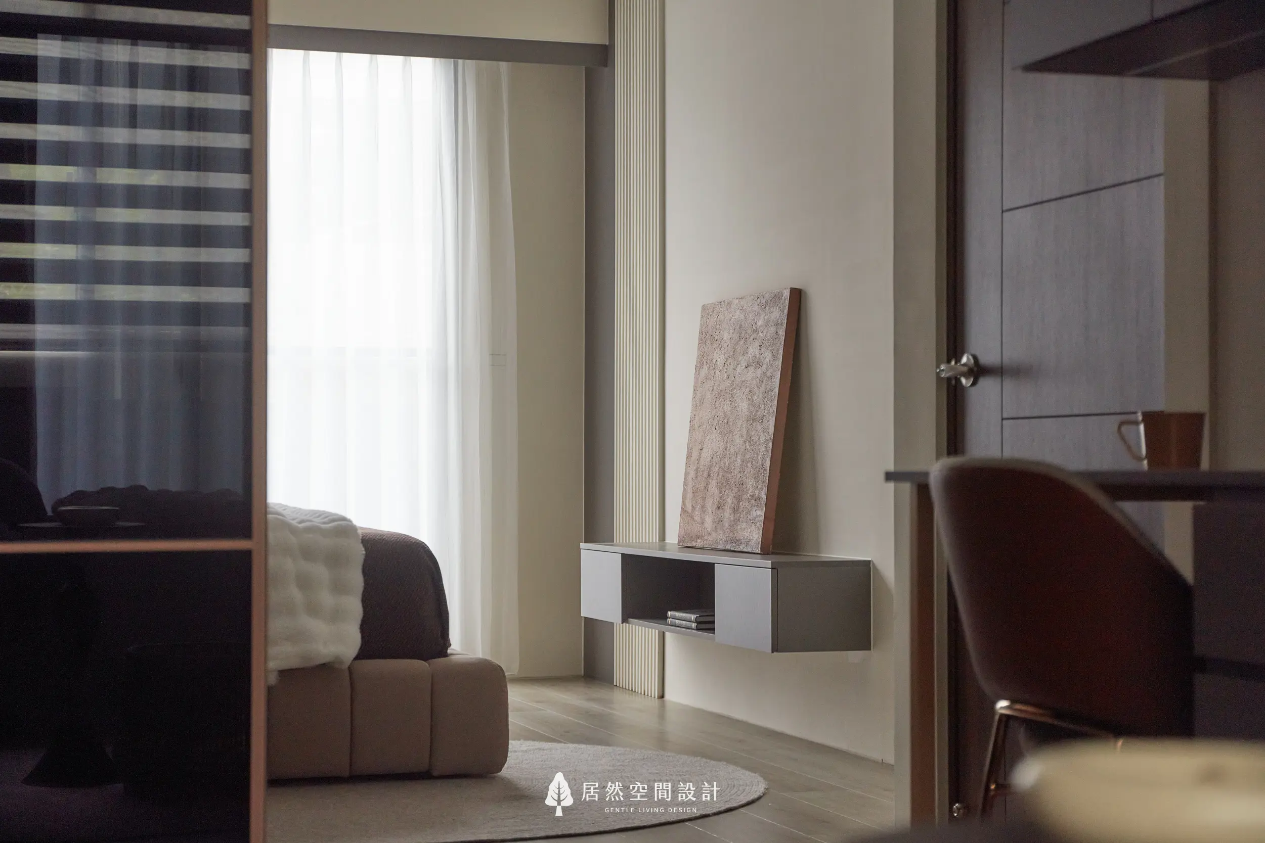 主臥室透過黑玻門片延伸視覺層次，米色軟包床尾與木地板鋪陳溫潤氛圍，窗邊紗簾引入柔和採光，營造沉靜休憩感