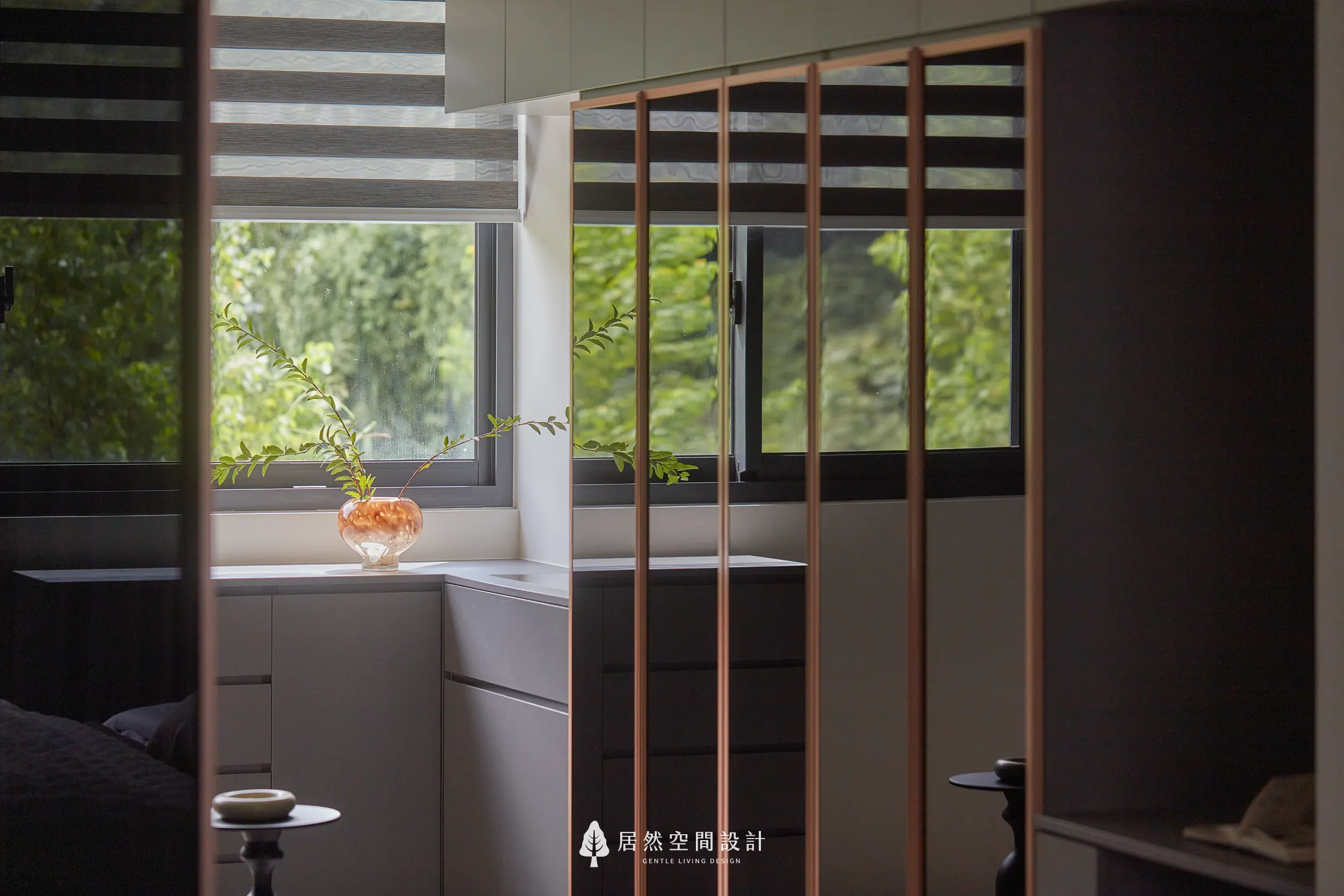 窗邊收納櫃與玻璃衣櫃門片形成層次界面，陶製花器與綠植點綴檯面，百葉窗引入自然光與戶外綠景，營造靜謐舒適的更衣空間