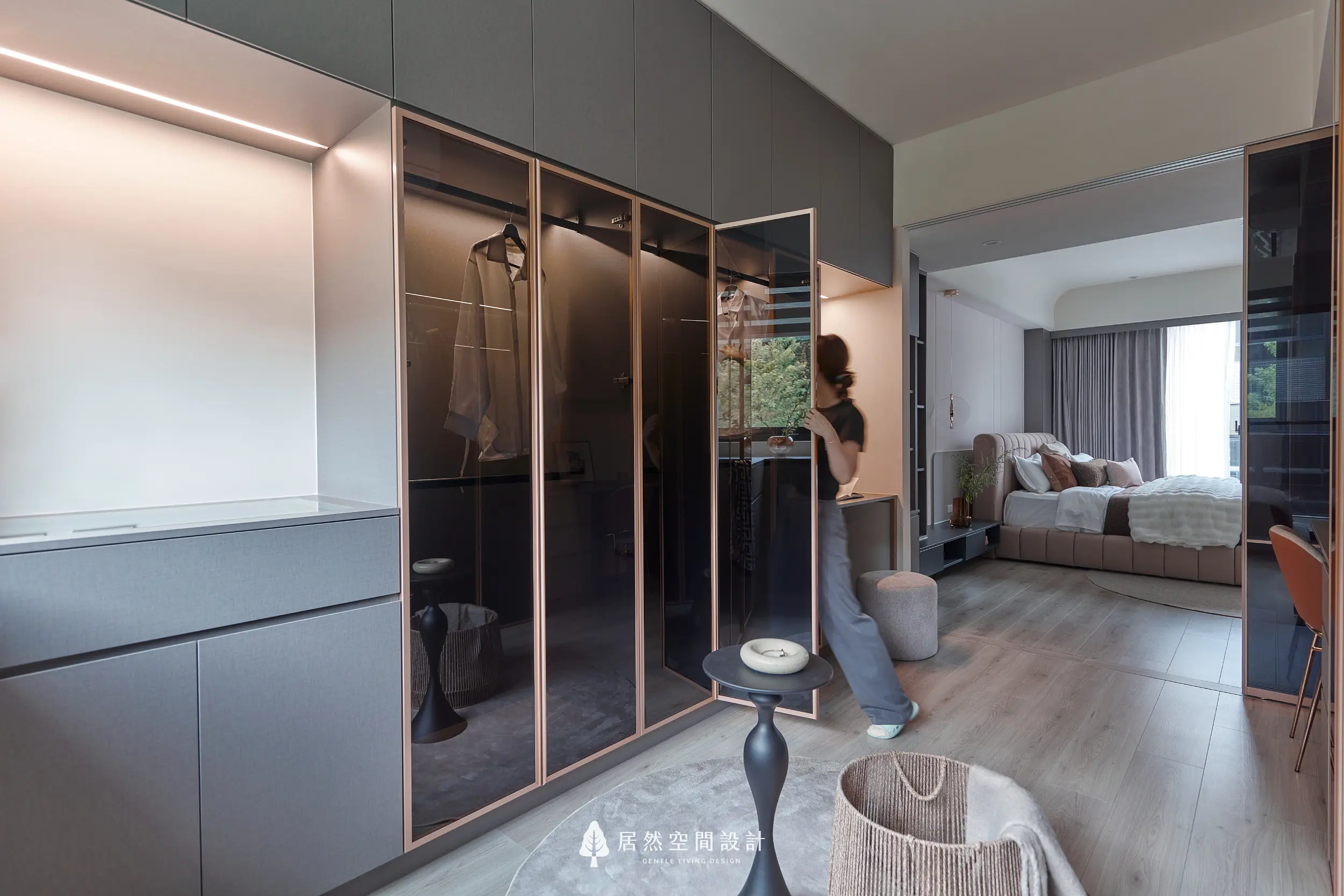 更衣室以玻璃衣櫃結合金屬框架打造展示式收納，吊掛與抽屜整合衣物整理機能，開放動線串聯主臥室空間，營造通透有序的更衣環境