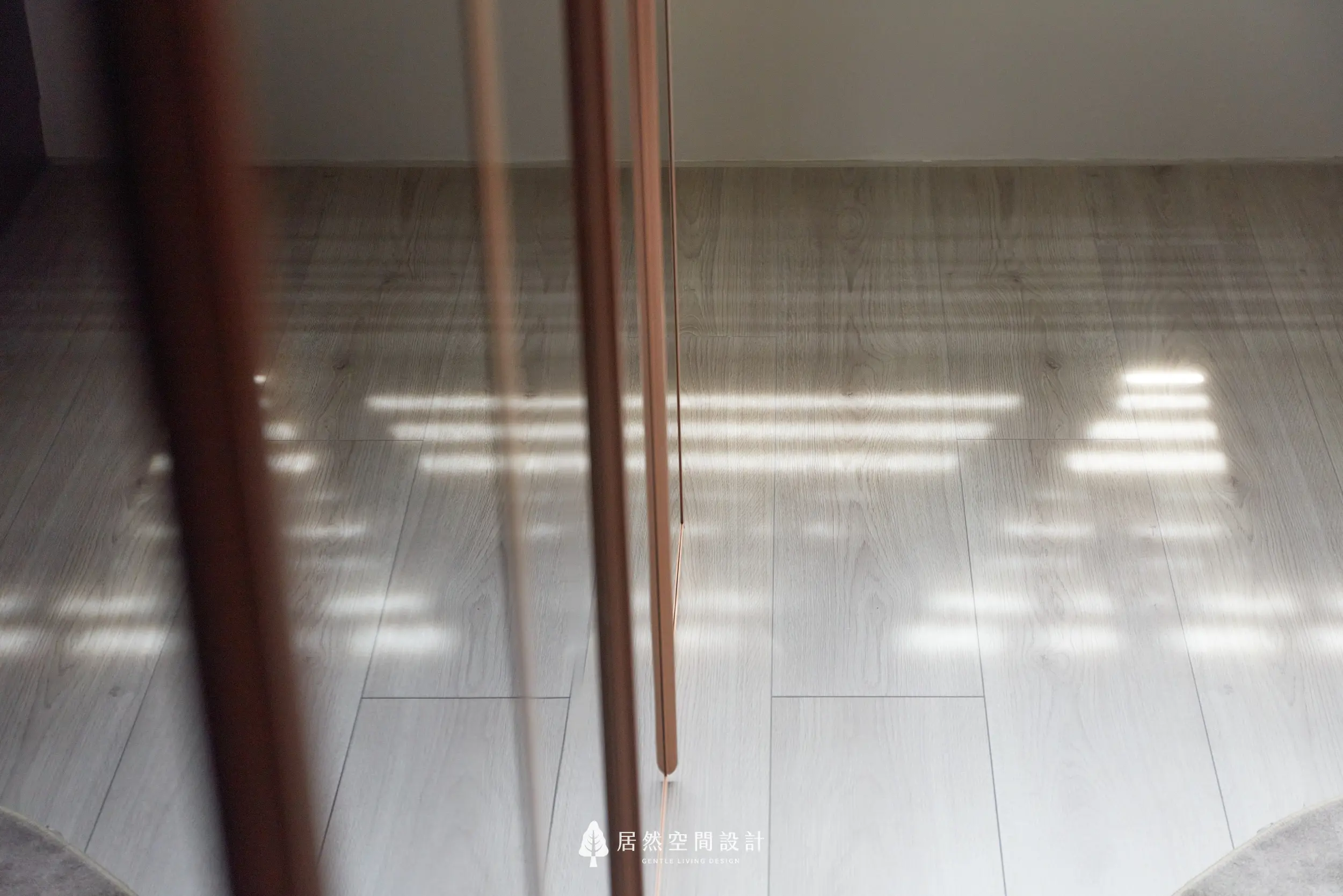 更衣室木地板鋪陳溫潤基調，玻璃衣櫃門片與金屬框架映射窗邊光影，調光簾自然光在地面形成層次紋理，營造安靜細膩的空間氛圍