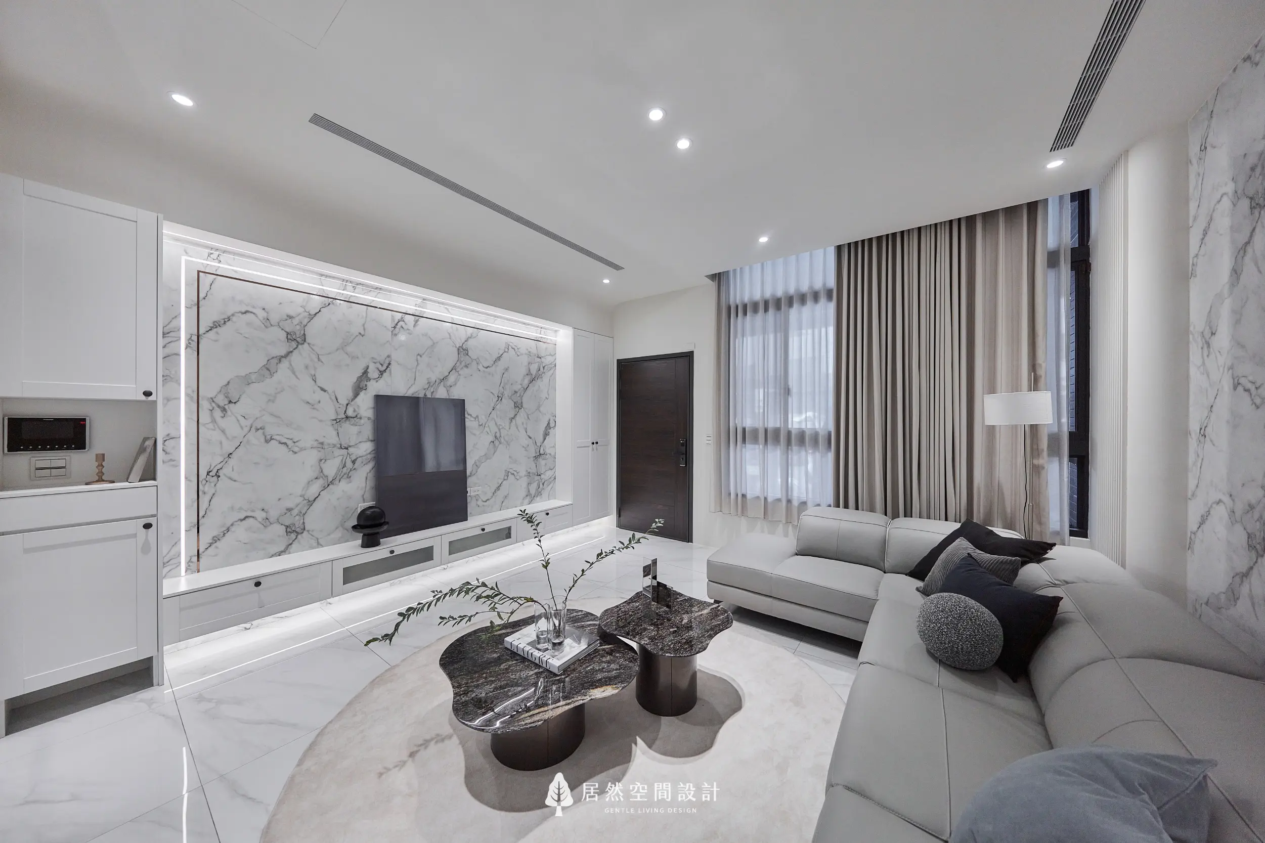 客廳以大理石紋理電視牆結合隱藏燈帶鋪陳視覺主軸，米色L型沙發與深色石紋茶几形成層次，大面窗簾柔化採光營造沉靜氛圍