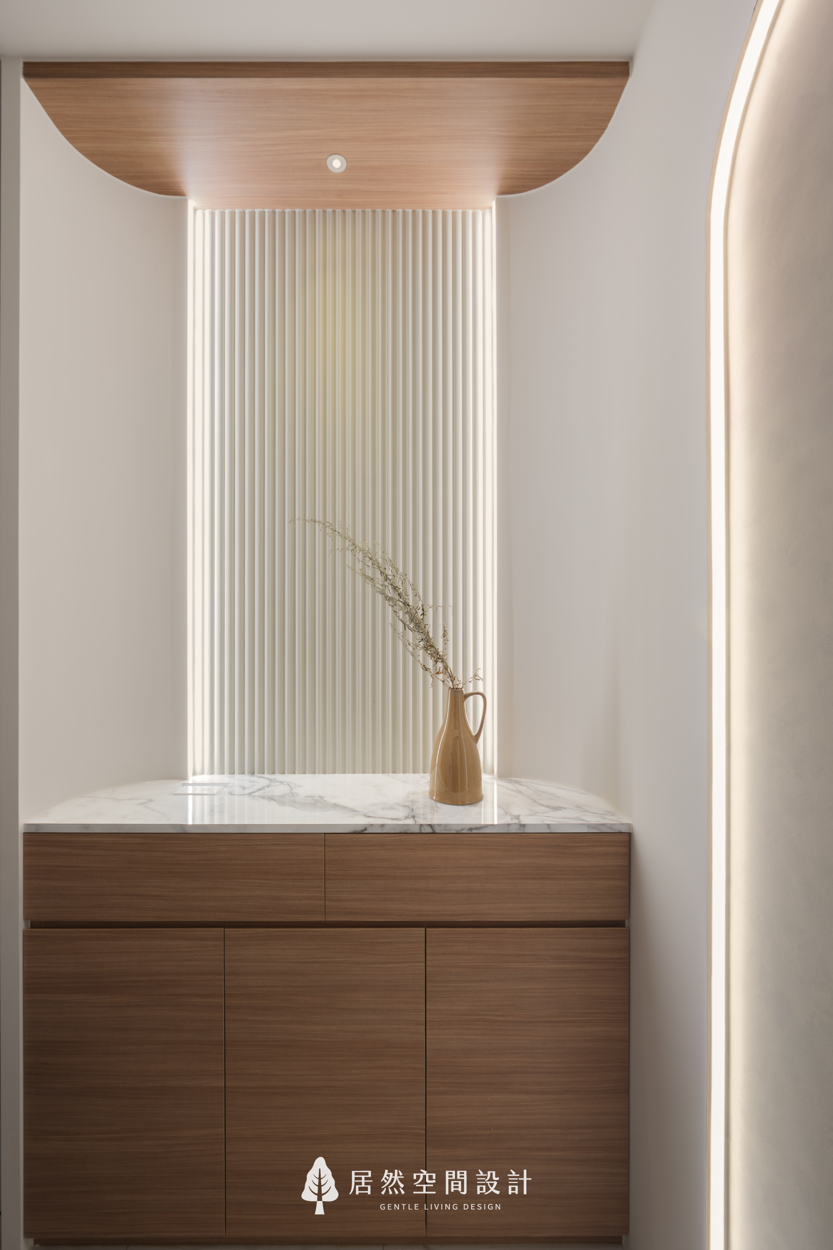 現代風室內設計進門端景，居然空間設計利用木紋矮櫃搭配大理石檯面，後方以淺色格柵板與柔和間接照明營造層次，圓弧天花設計展現迎賓質感。