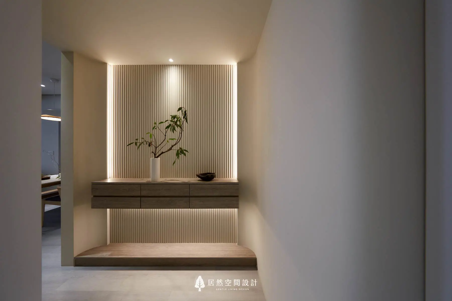 玄關端景格柵背板，結合兩側垂直燈帶與懸浮櫃下方光源，展現居家空間感。透過細膩的間接照明，讓轉角牆面光影更加柔和、具有豐富視覺層次。