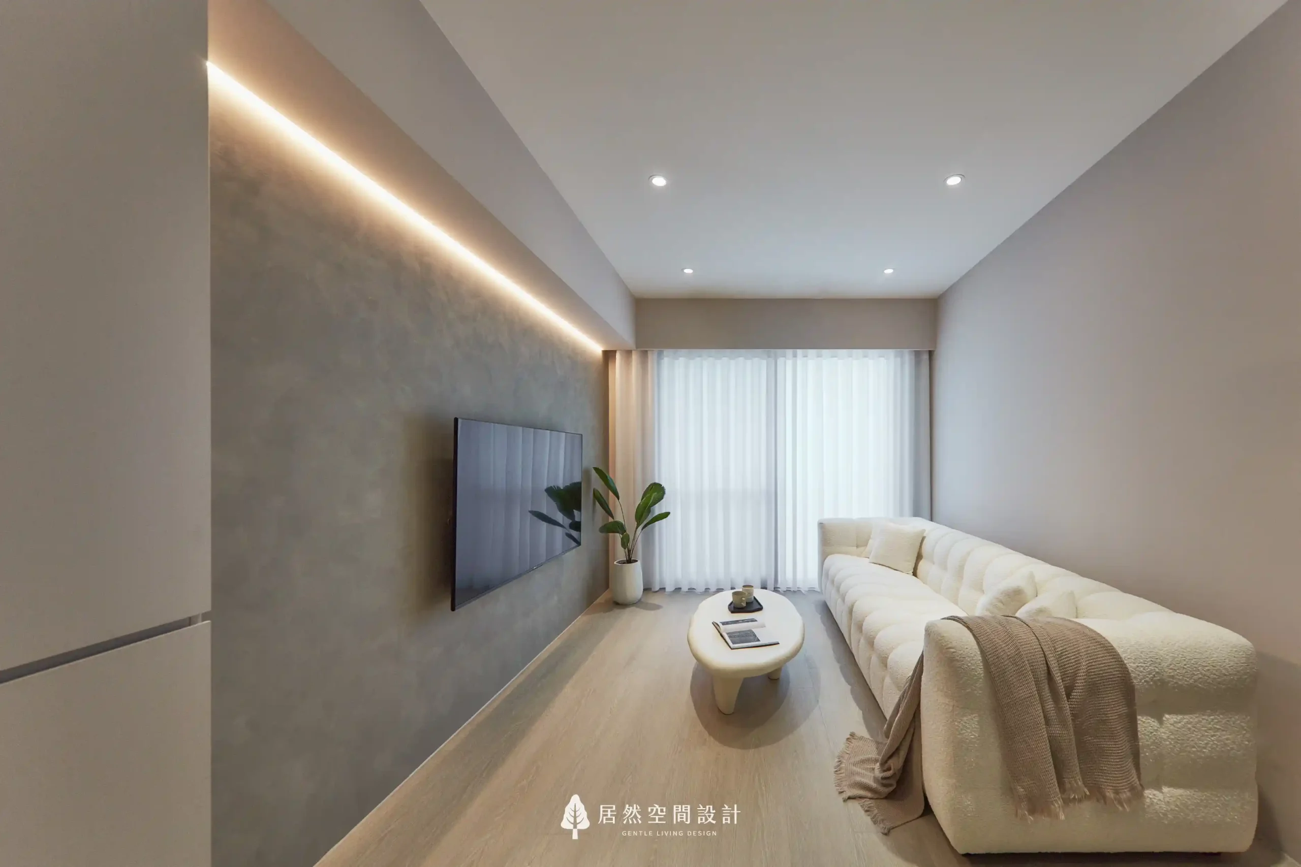 客廳電視牆採用灰色藝術塗料，天花板設計燈槽裝設間接照明，光線柔和地灑落，搭配米白色沙發與落地窗，營造出舒適且具有質感的生活氛圍。