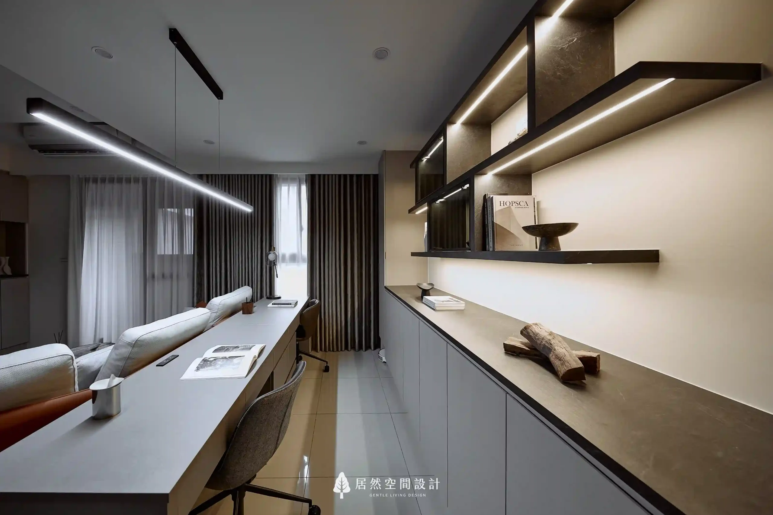 開放式書房展示層架內嵌燈條，展現俐落線條感。層架上的間接照明設計不僅能點亮收藏品，更成功為居家閱讀區增添沉靜且知性的空間層次。